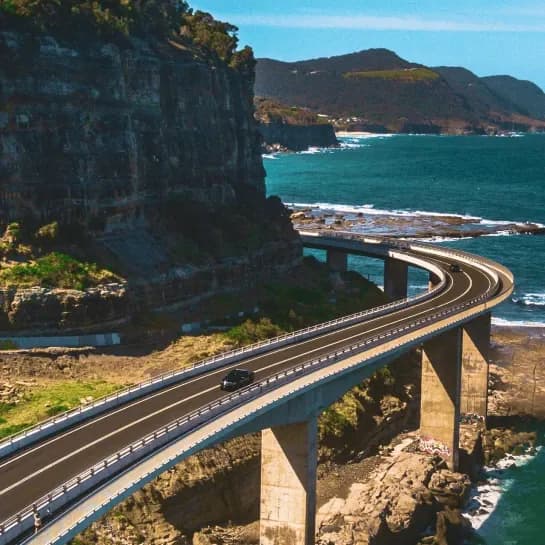 Car on curved coastal bridge